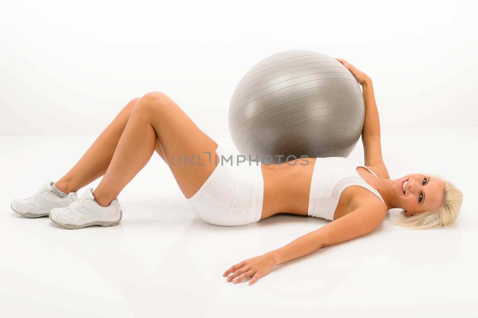 Fitness blonde woman exercising with gym ball lying white floor