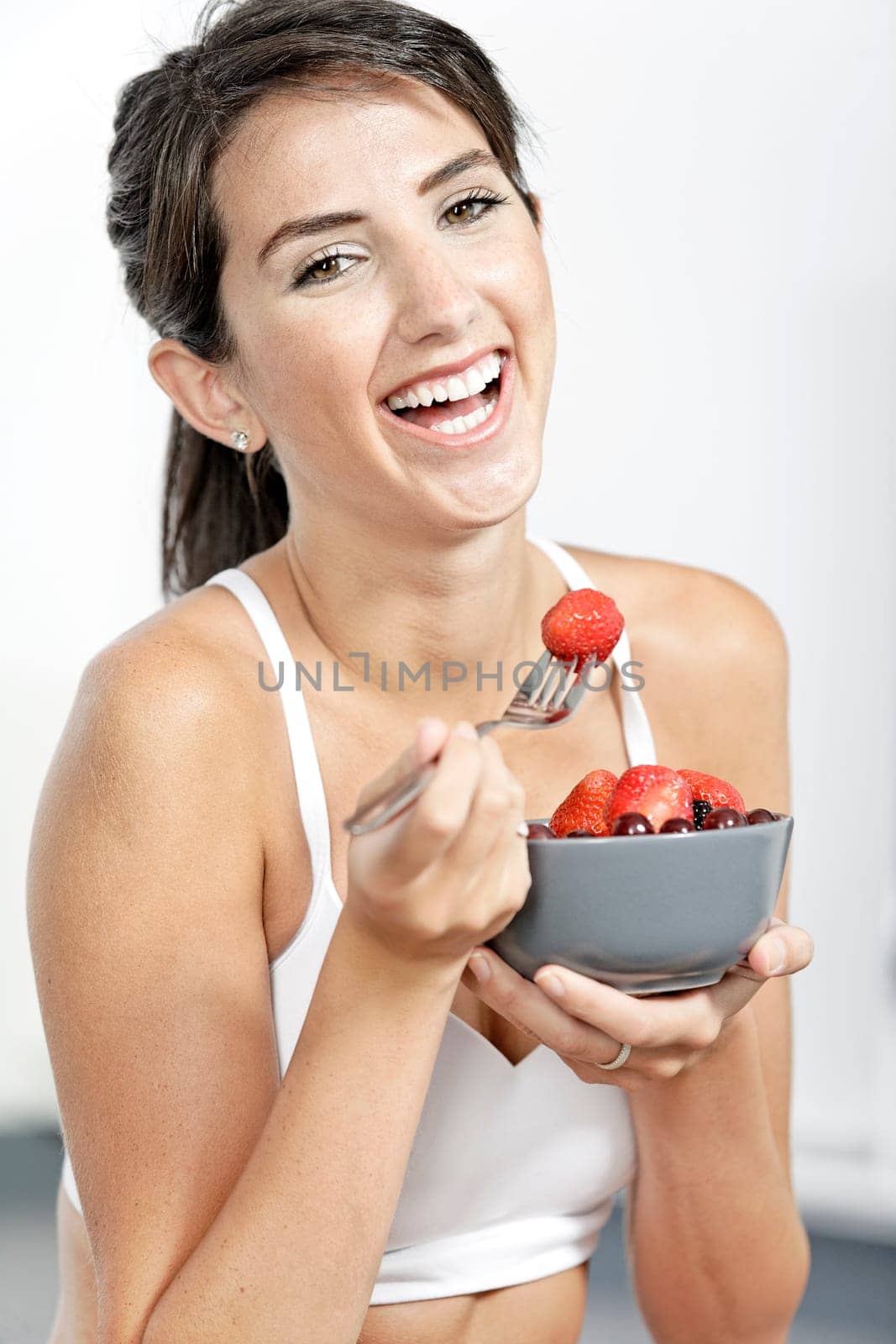 beautiful young woman in fitness clothes eating fresh fruit from a bowl at home