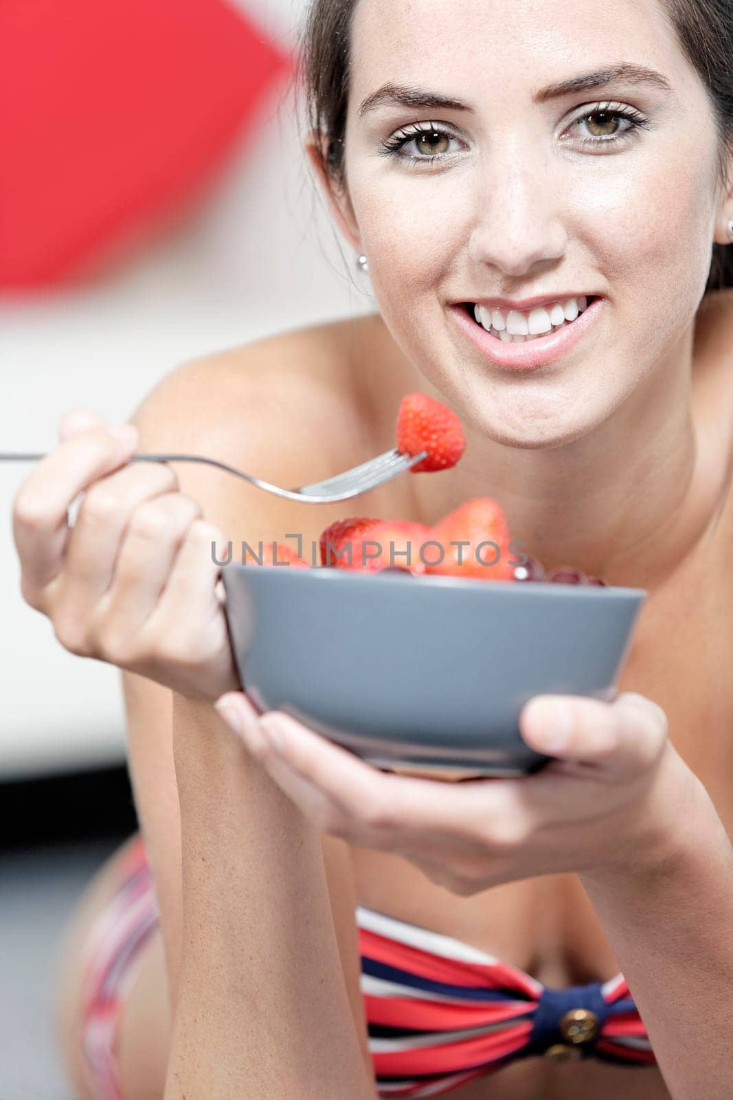 Beautiful young woman enjoying fresh fruit for breakfast in a red bikini