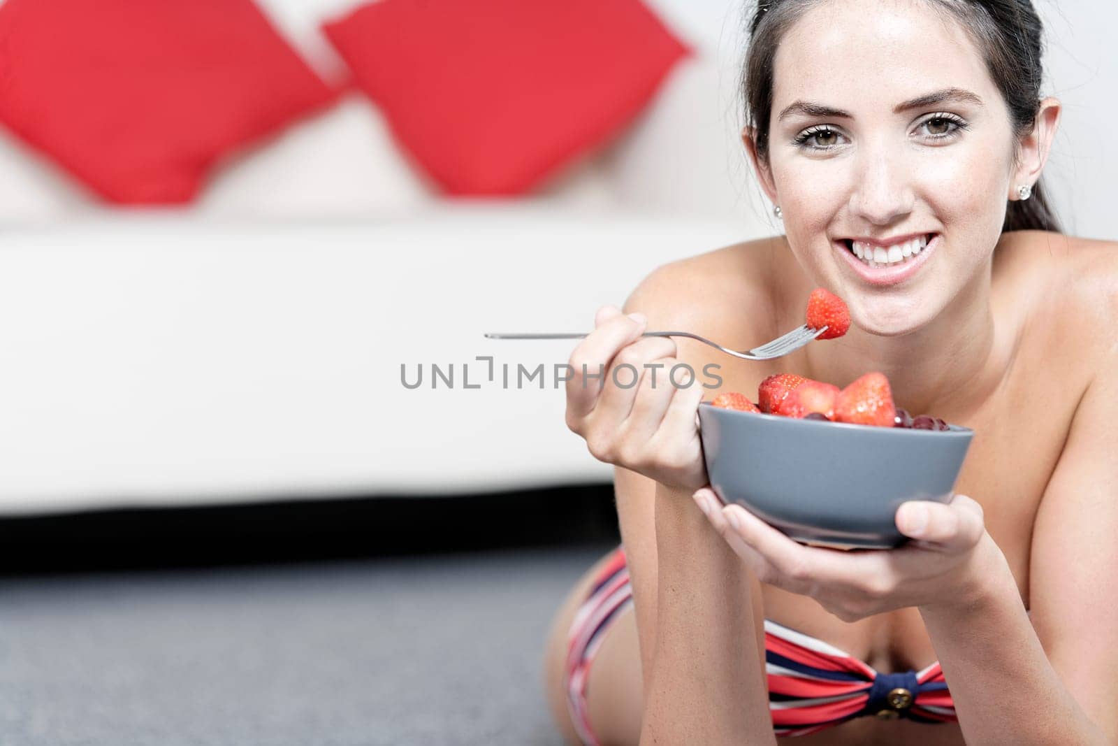 Beautiful young woman enjoying fresh fruit for breakfast in a red bikini