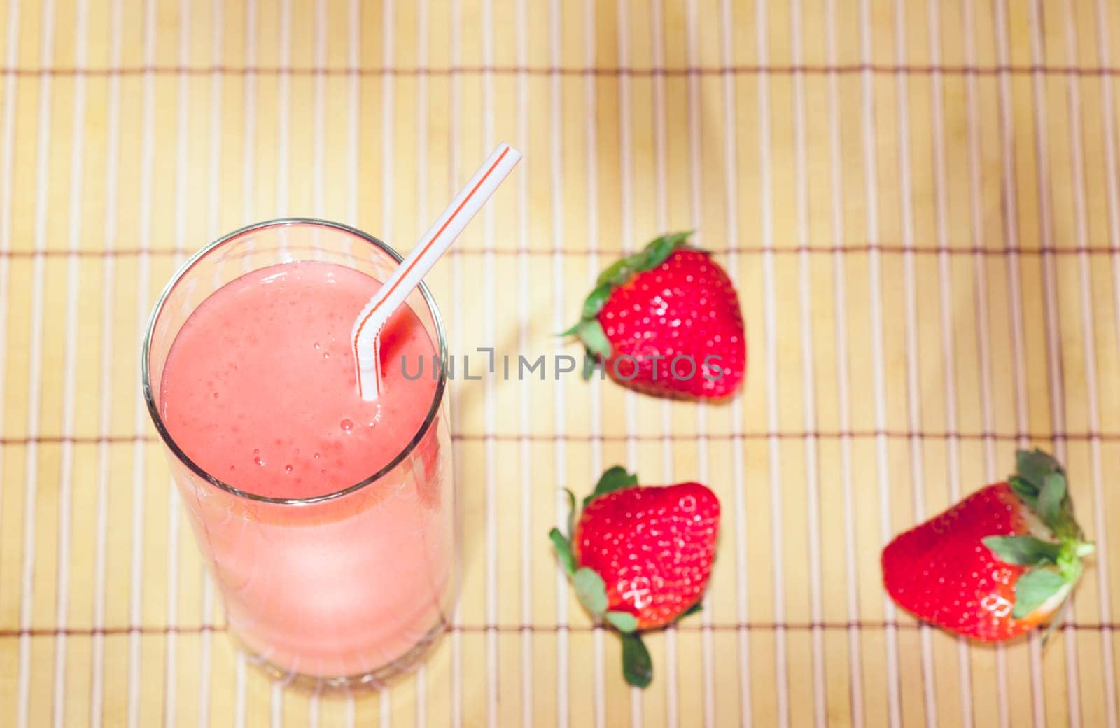 Fresh strawberry smoothie in a glass with berries next to it