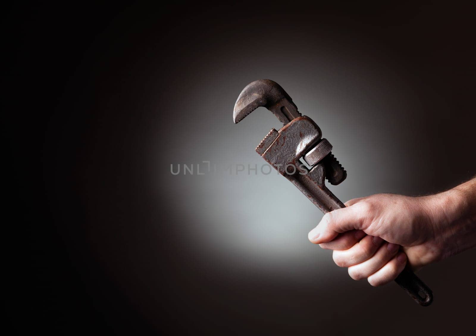 A man&#039 s hand holding a pipe wrench highlighted against a black background