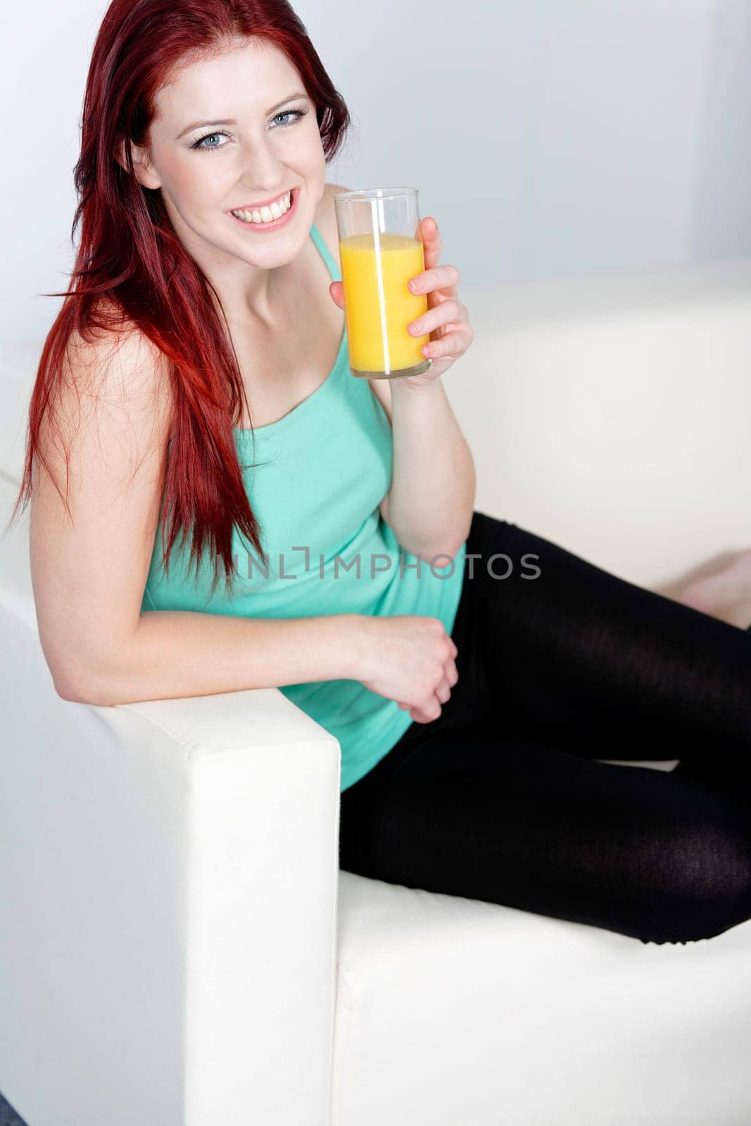 Happy smiling young woman drinking fresh Orange juice at home on the sofa