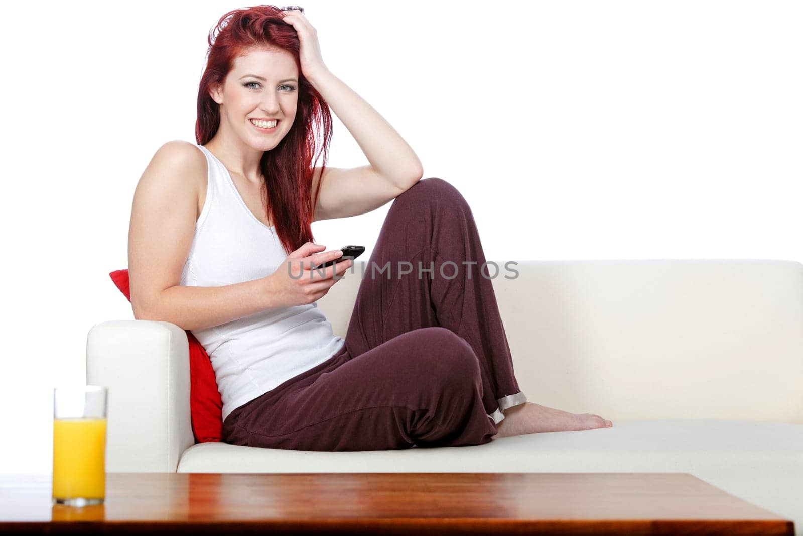 happy young woman sat on her white sofa at home smiling at text messages on her phone