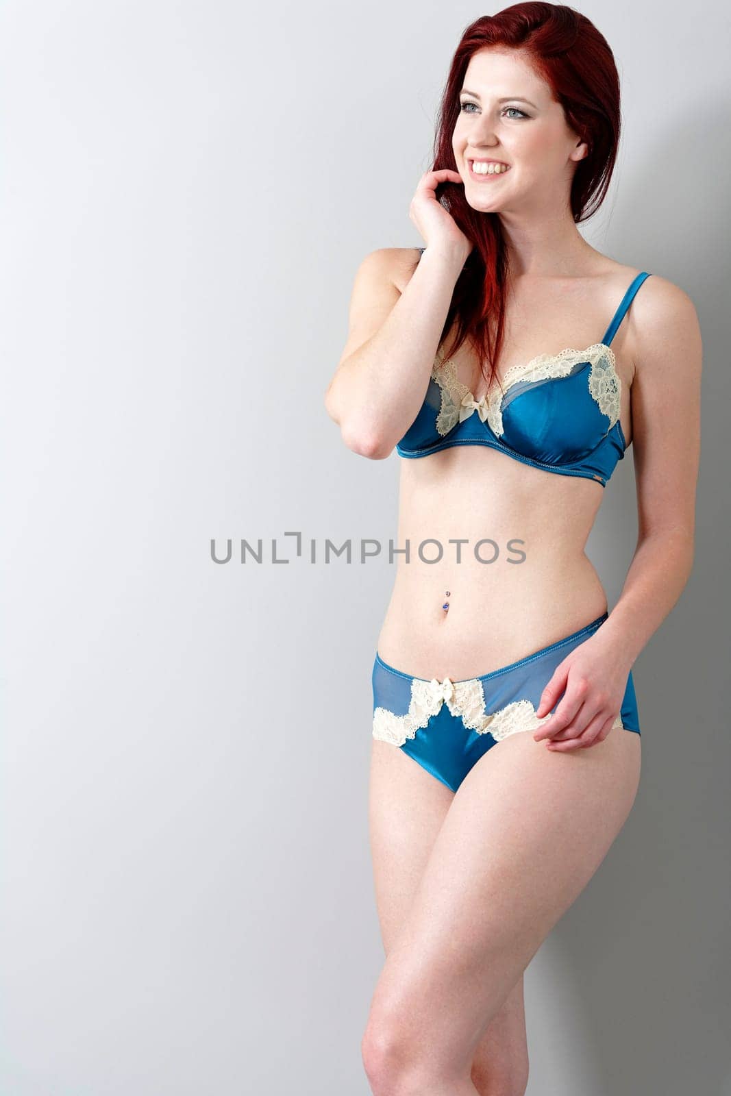 Sexy young woman in blue underwear leaning against a wall at home.