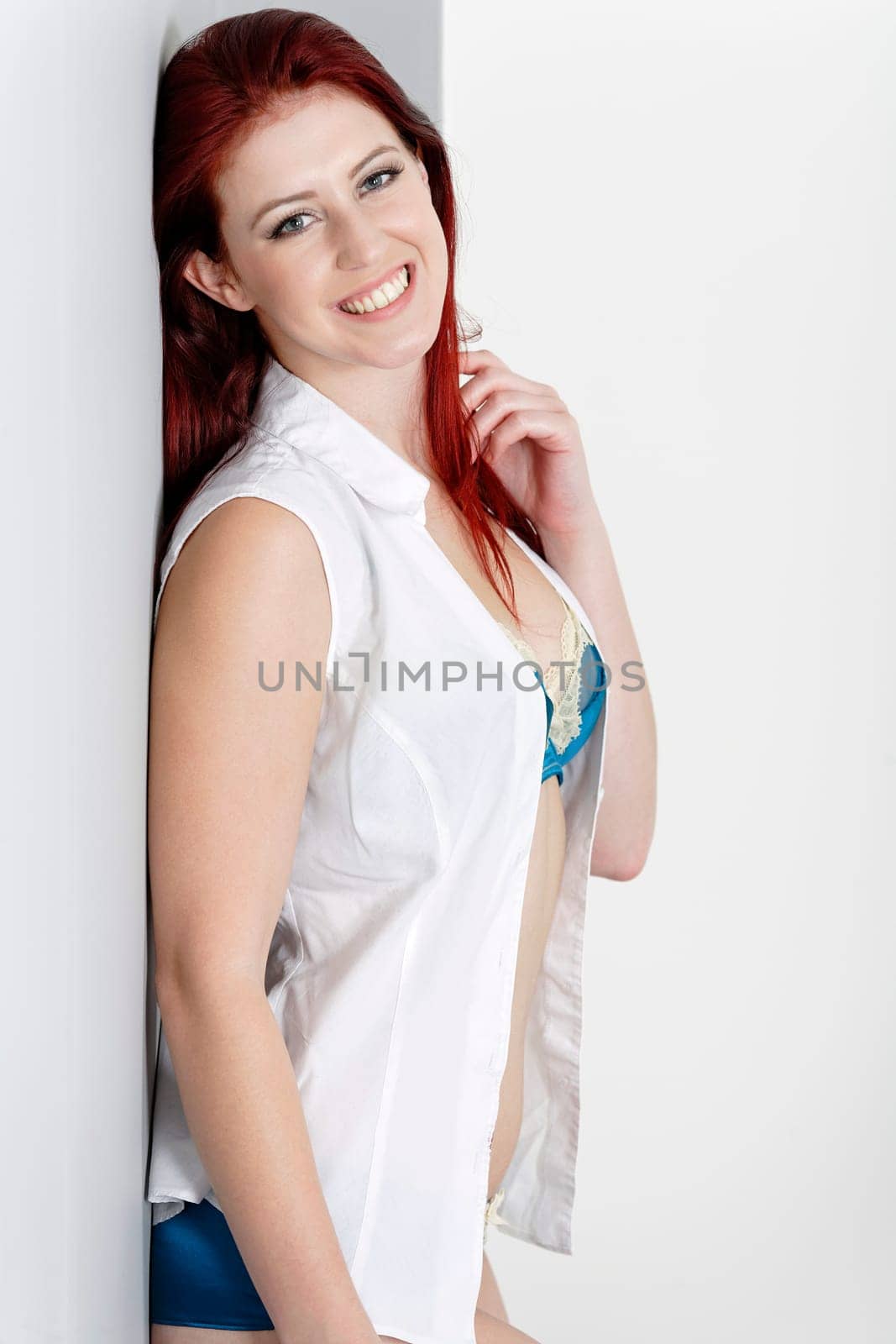 Smiling beautiful woman in blue underwear and white shirt leaning against a wall