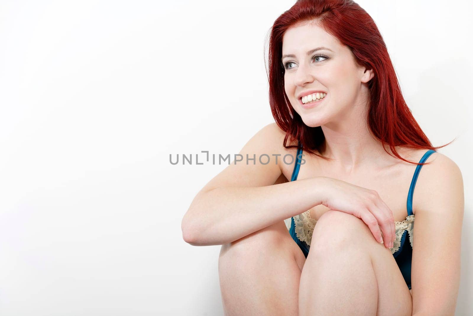 Sexy young woman in blue underwear sitting against a wall at home.