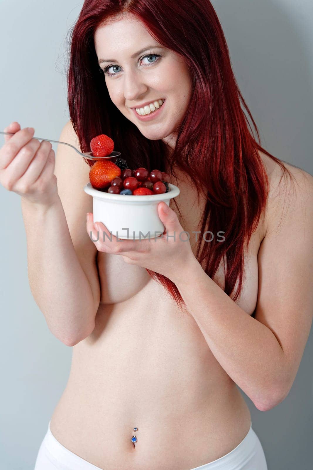 Happy young woman eating a bowl of fresh fruit in her underwear at home