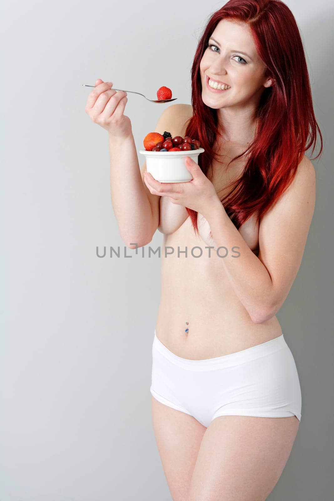 Happy young woman eating a bowl of fresh fruit in her underwear at home