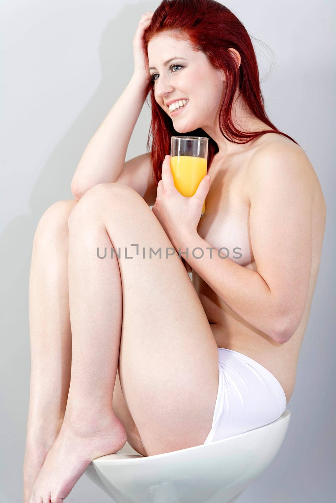 beautiful young woman sat on a stool with a glass of fresh Orange juice in her underwear.