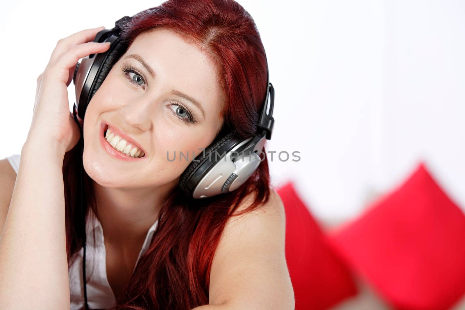 Beautiful young woman lying on her sofa at home listening to music on her headphones
