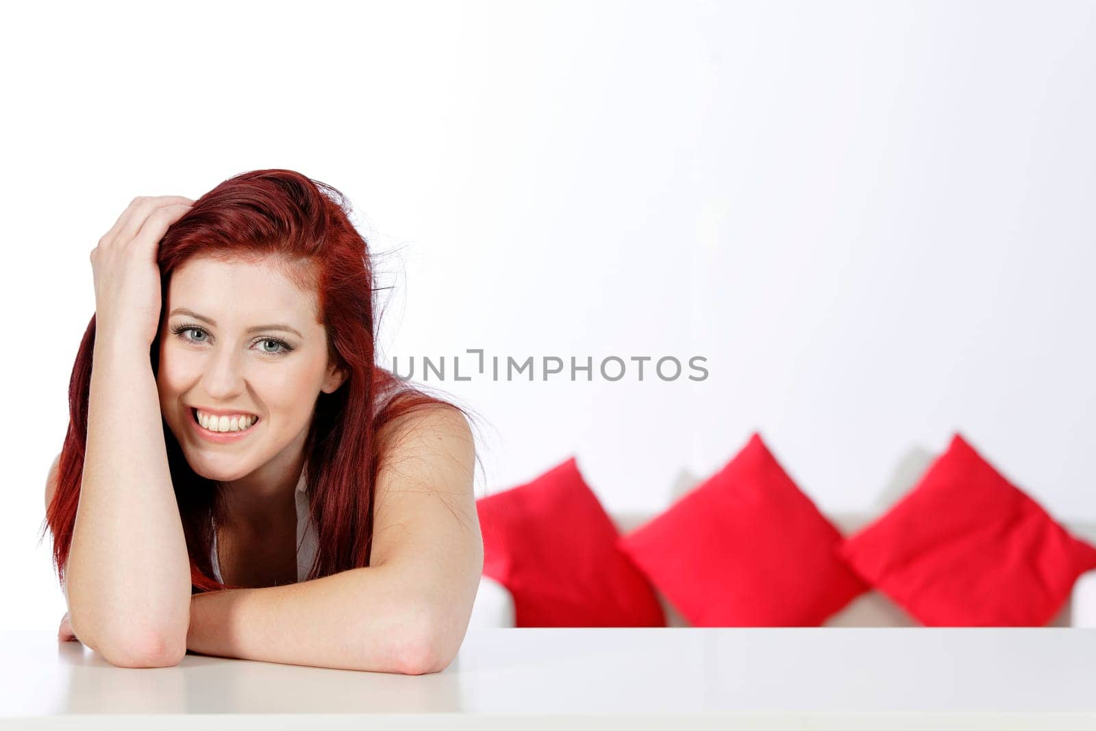 Beautiful young woman leaning on a table at home with a sofa in the background.