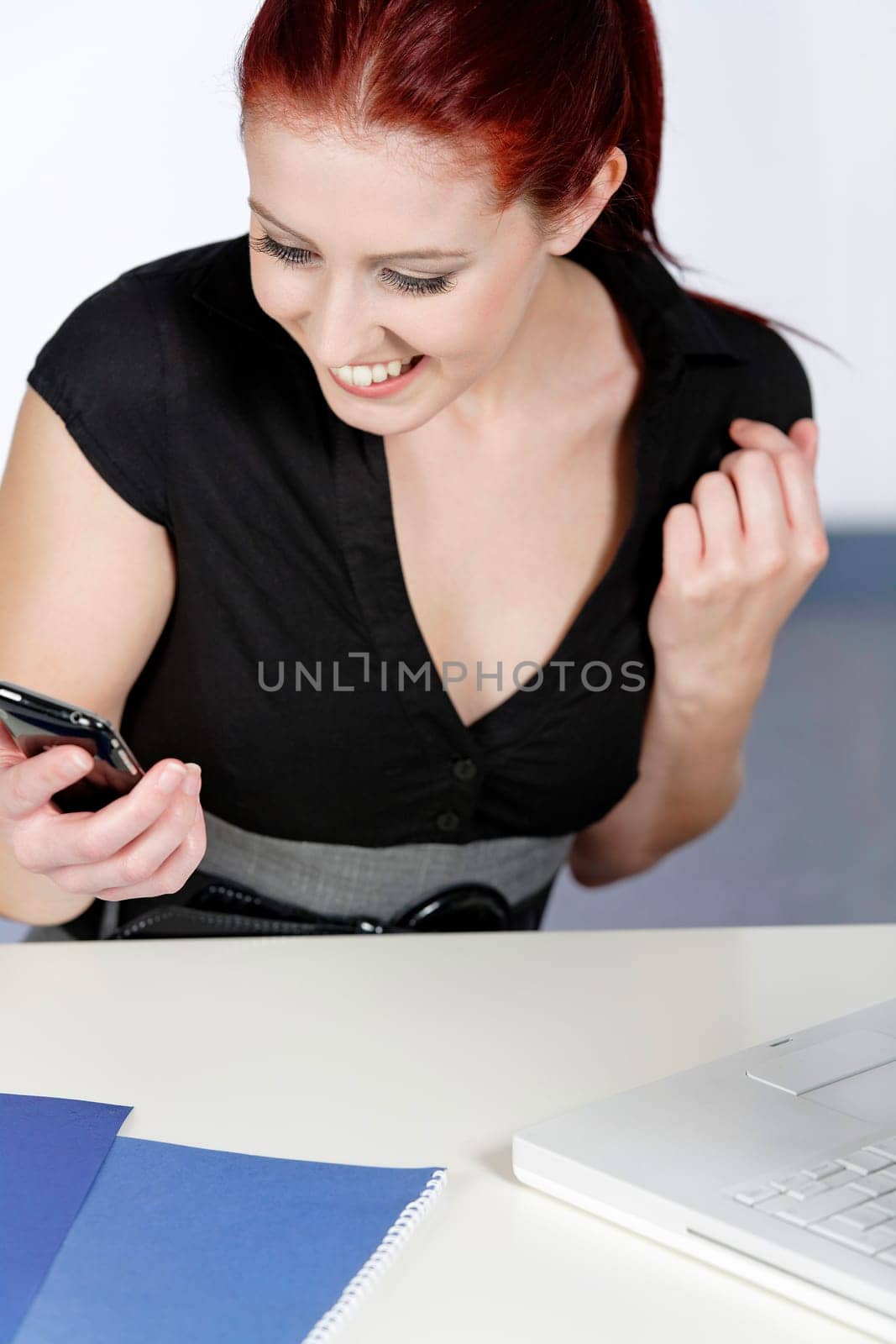 Professional young woman receiving good news on her mobile at work