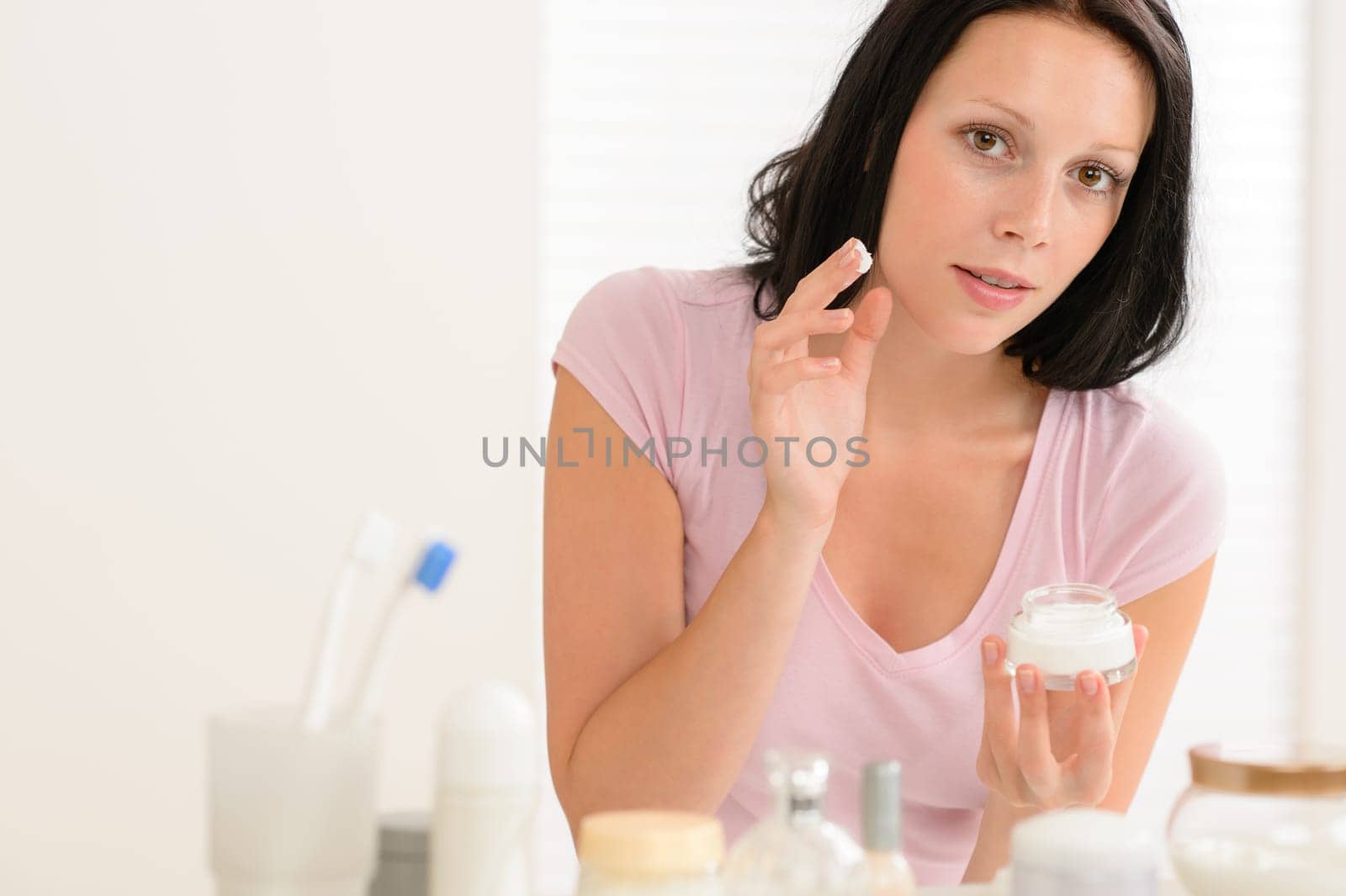 Beauty woman putting facial cream in front of bathroom mirror