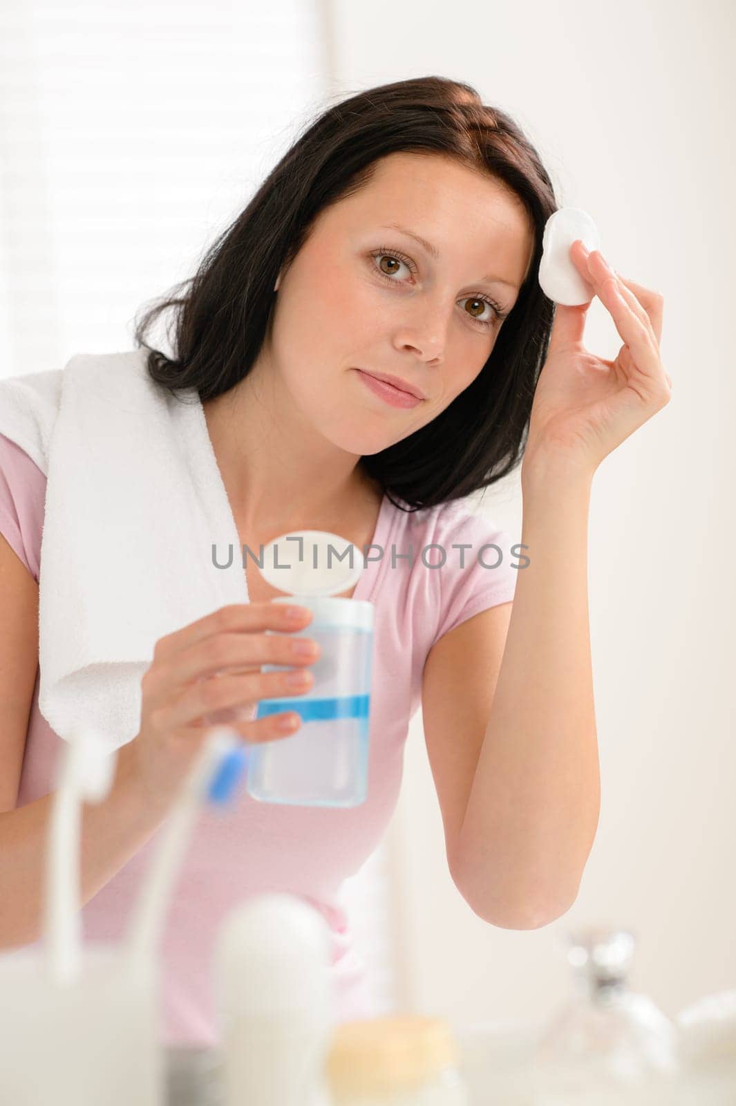 Young brunette woman face tonic cleaning with cotton pad bathroom