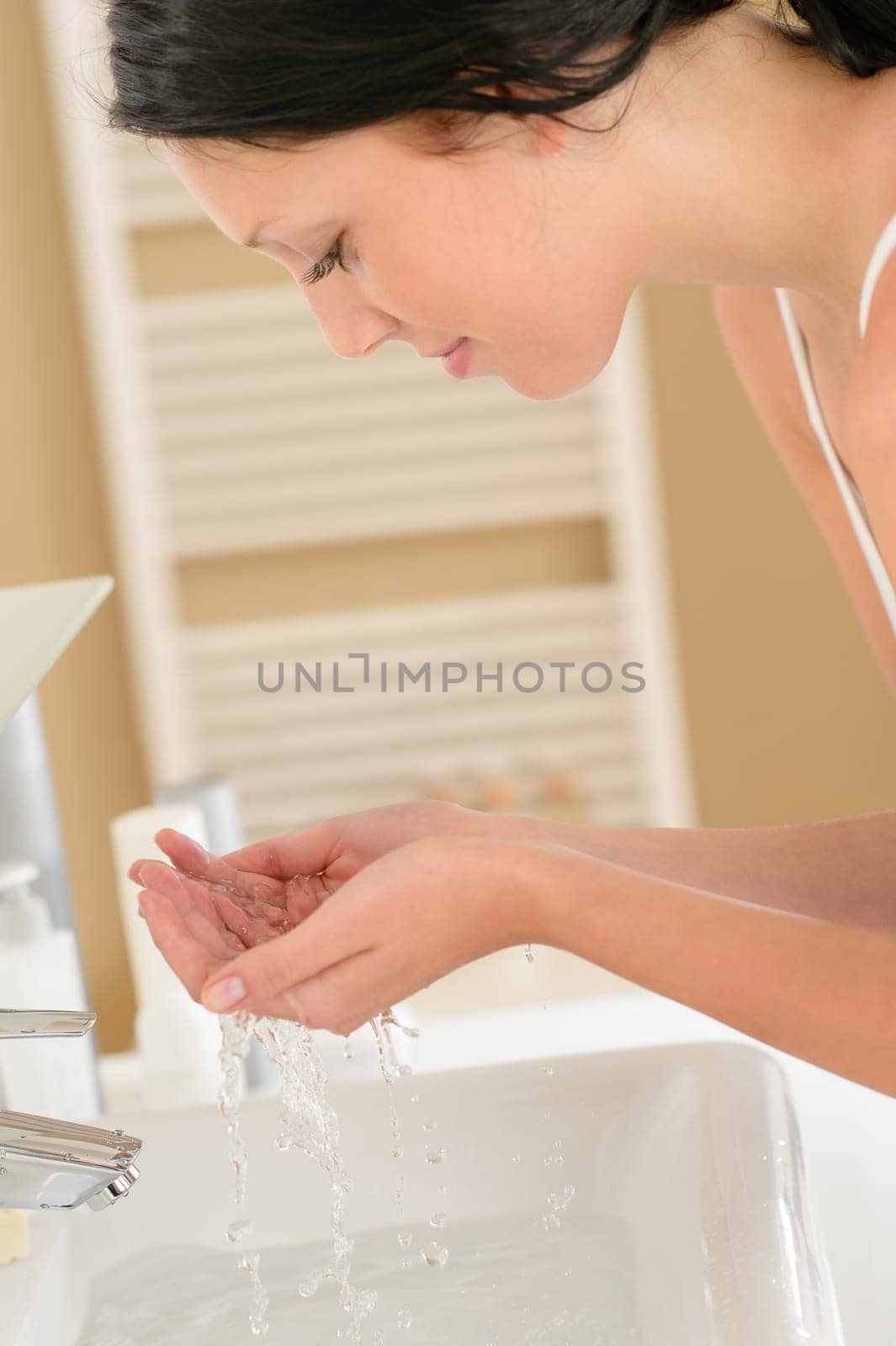 Young woman in bathroom washing her face at wash basin