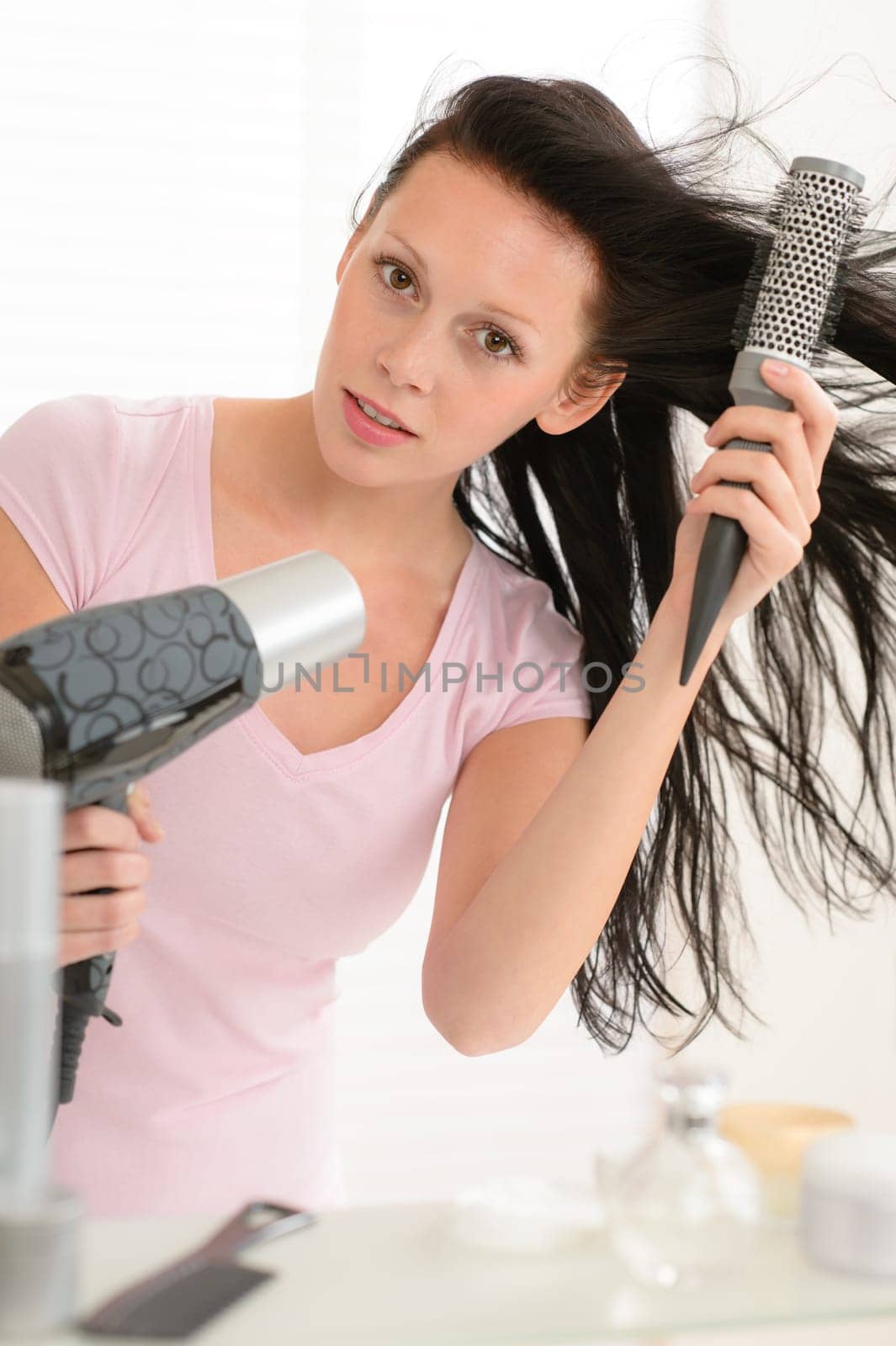 Brunette woman blow-drying long hair using round hairbrush