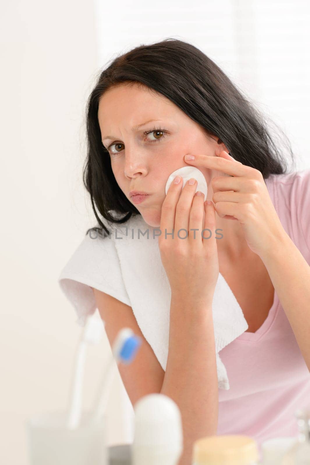 Young brunette woman in bathroom squeezing pimple cleaning acne skin