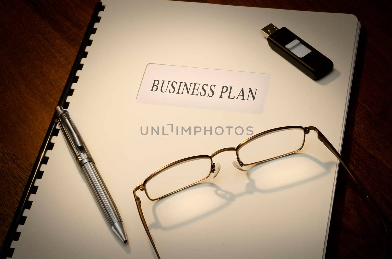 Business Plan on a desk wiht a pen, a thumb drive and a pair of glasses
