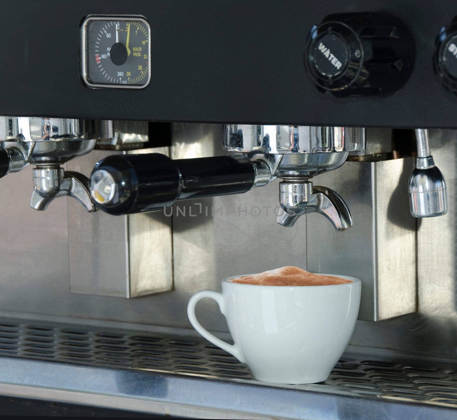 Coffee cup filled with cappuccino coffee, sitting on the tray of a commercial espresso machine