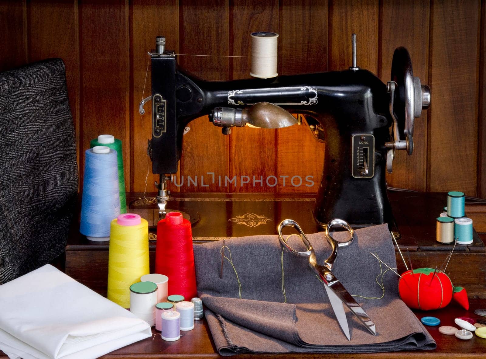 Retro sewing machine with sewing paraphernalia including thread, fabric, sewing needles, pin cushion, buttons scissors and thimble