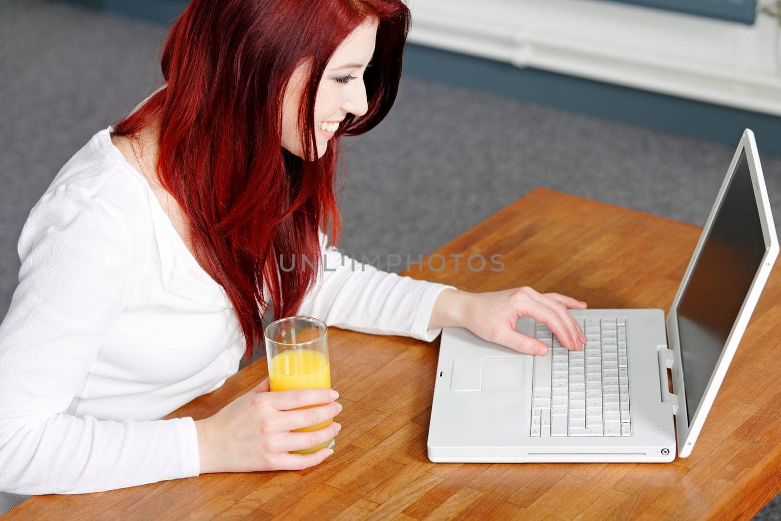 Beautiful young woman using a laptop at home with a fresh glass of Orange juice.