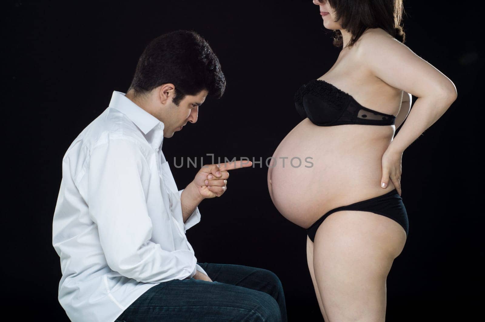 Young father pointing finger at wife&#039 s baby belly.