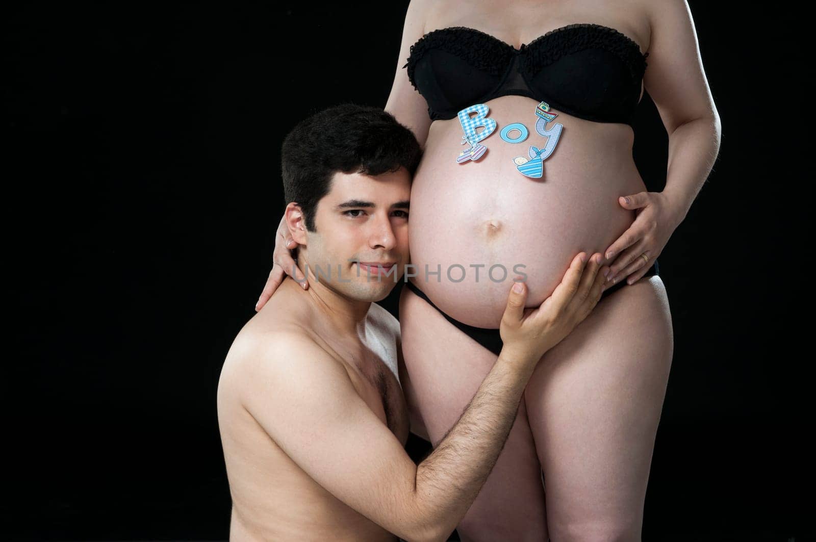 Portrait of young father listening to baby belly with the word boy on it.