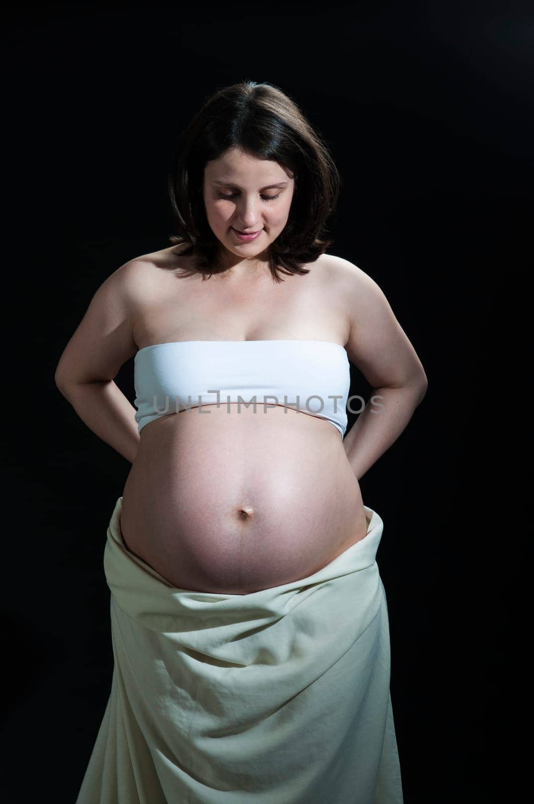 Portrait of happy young pregnant woman looking at her baby belly.