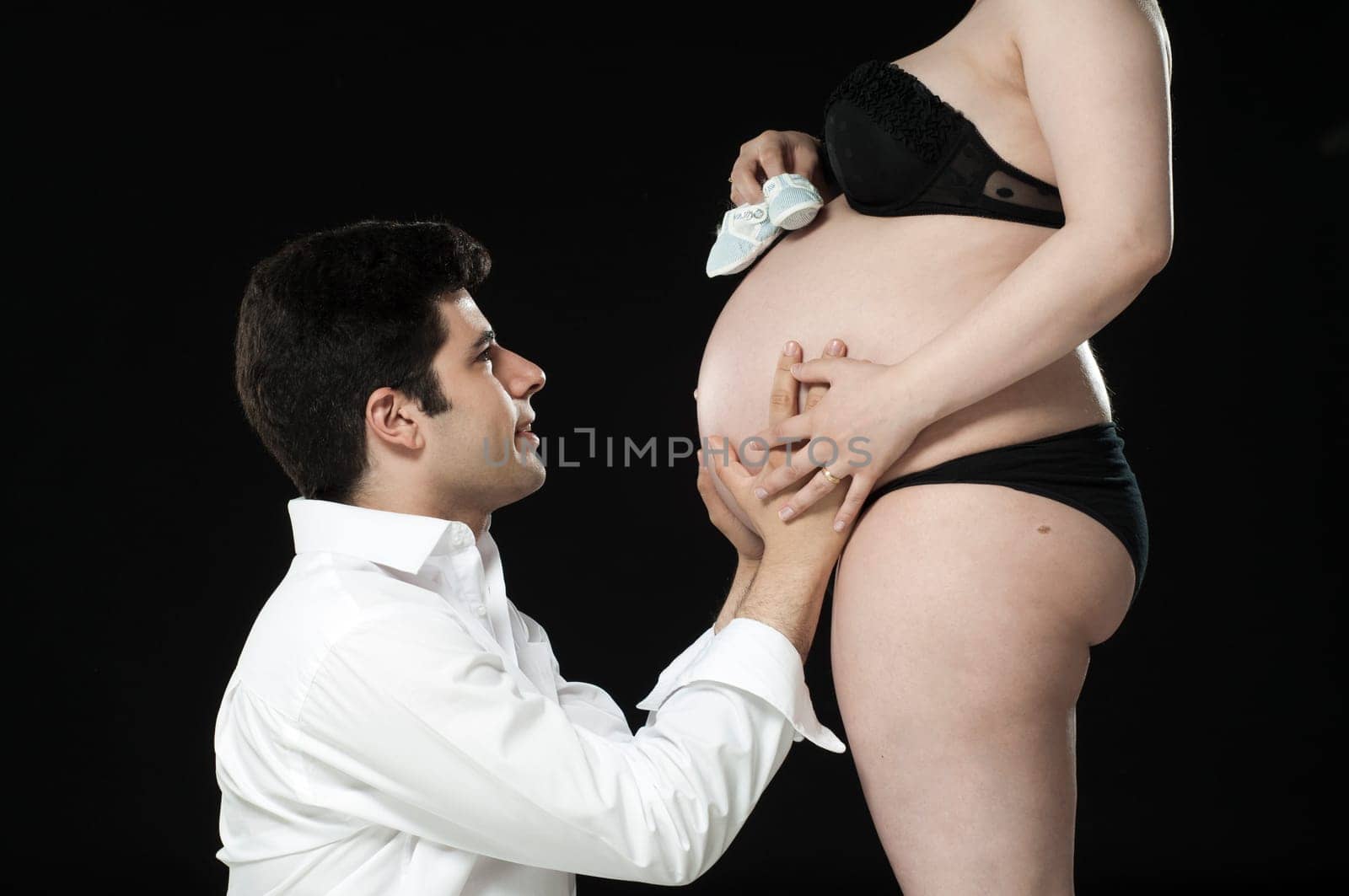 Portrait of young father looking at baby shoes on wife&#039 s baby belly.