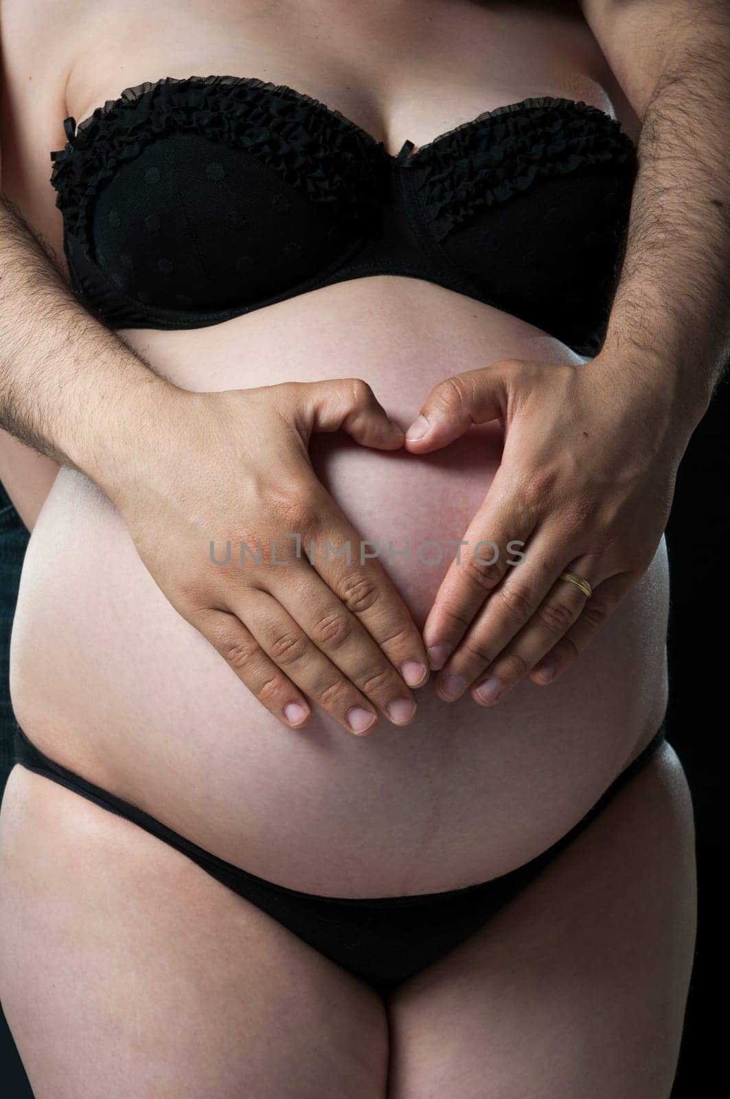 Cropped shot of man making shape of heart on wife&#039 s baby belly.