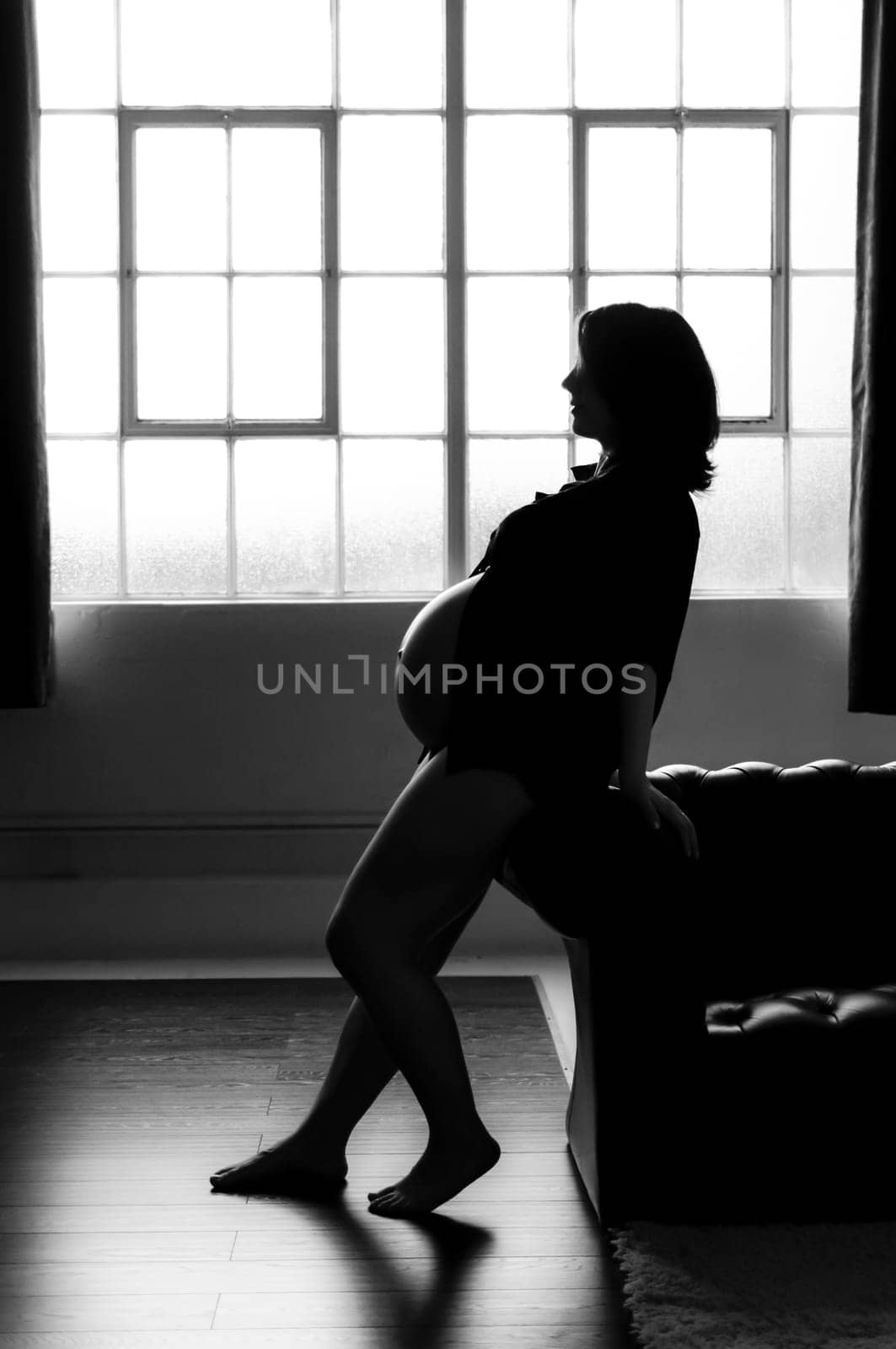 Black and white silhouette of pregnant woman leaning against sofa.