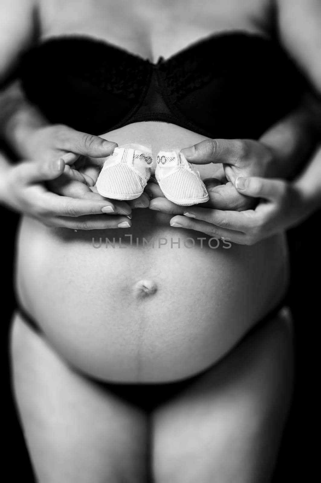 Shallow depth of field cropped shot of pregnant woman holding baby shoes with husband. Hands and belly only.