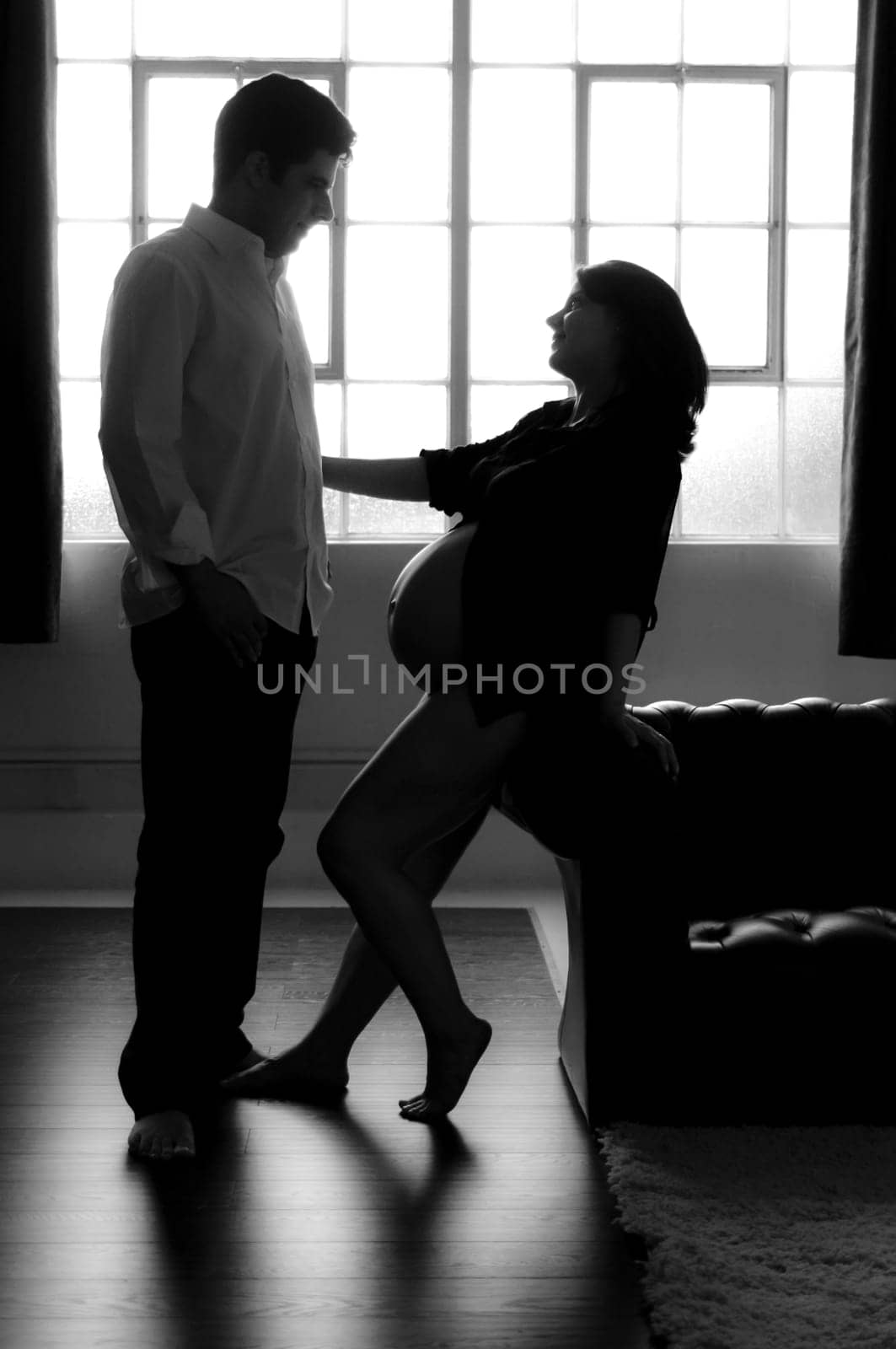 Black and white silhouette of pregnant woman reaching out for her husband.