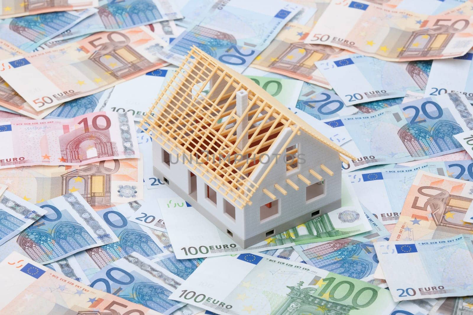 Building cost (construction cost) concept. Model of house under construction (rough construction) and money.