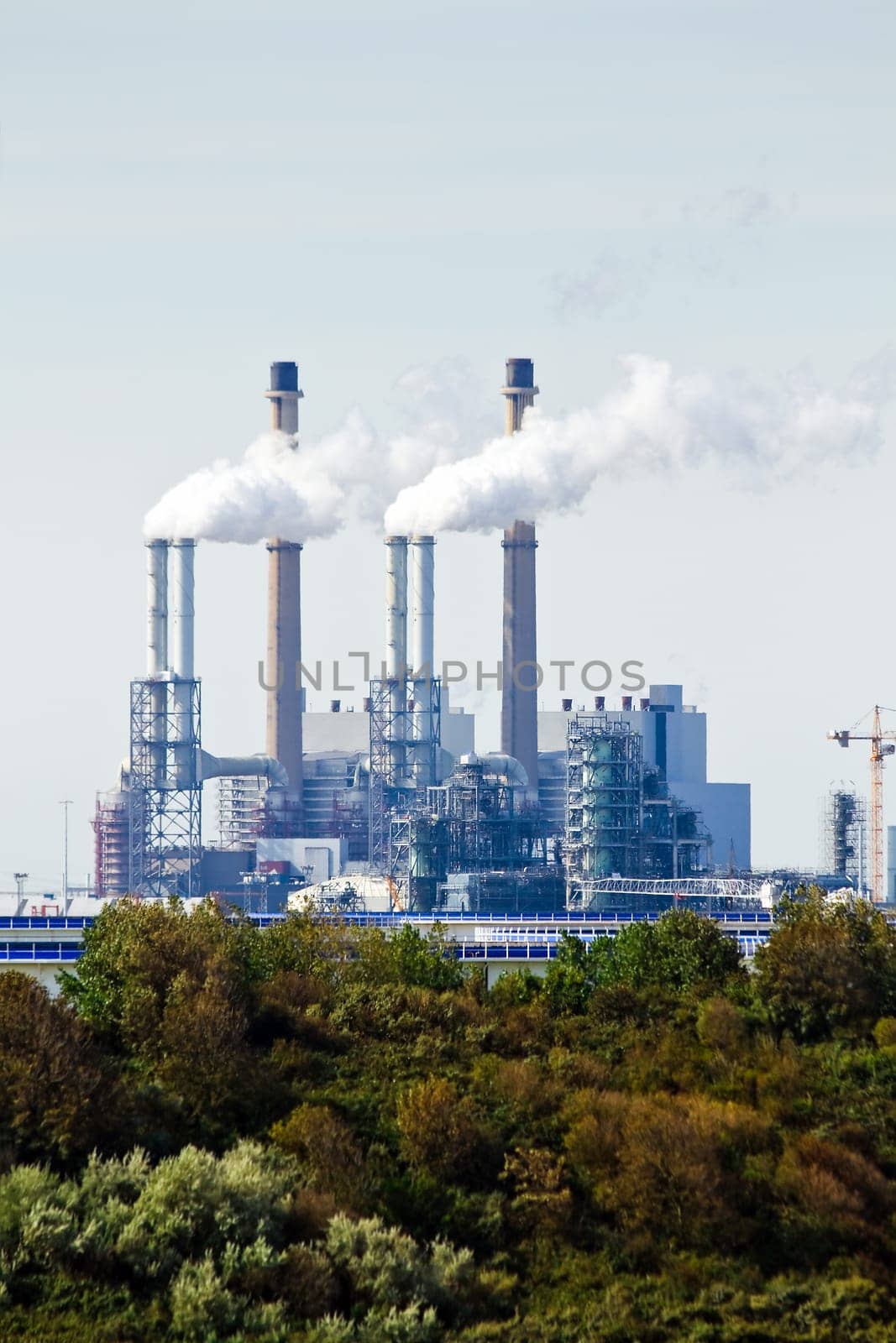 Industrial building and pollution in background and trees in foreground