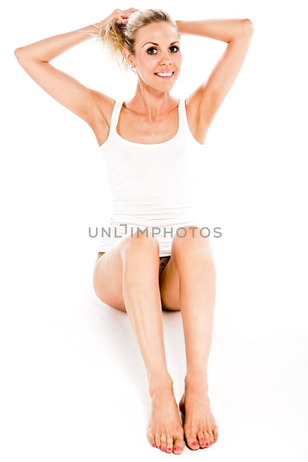 Attractive young woman in a white vest top sitting on the floor on white background