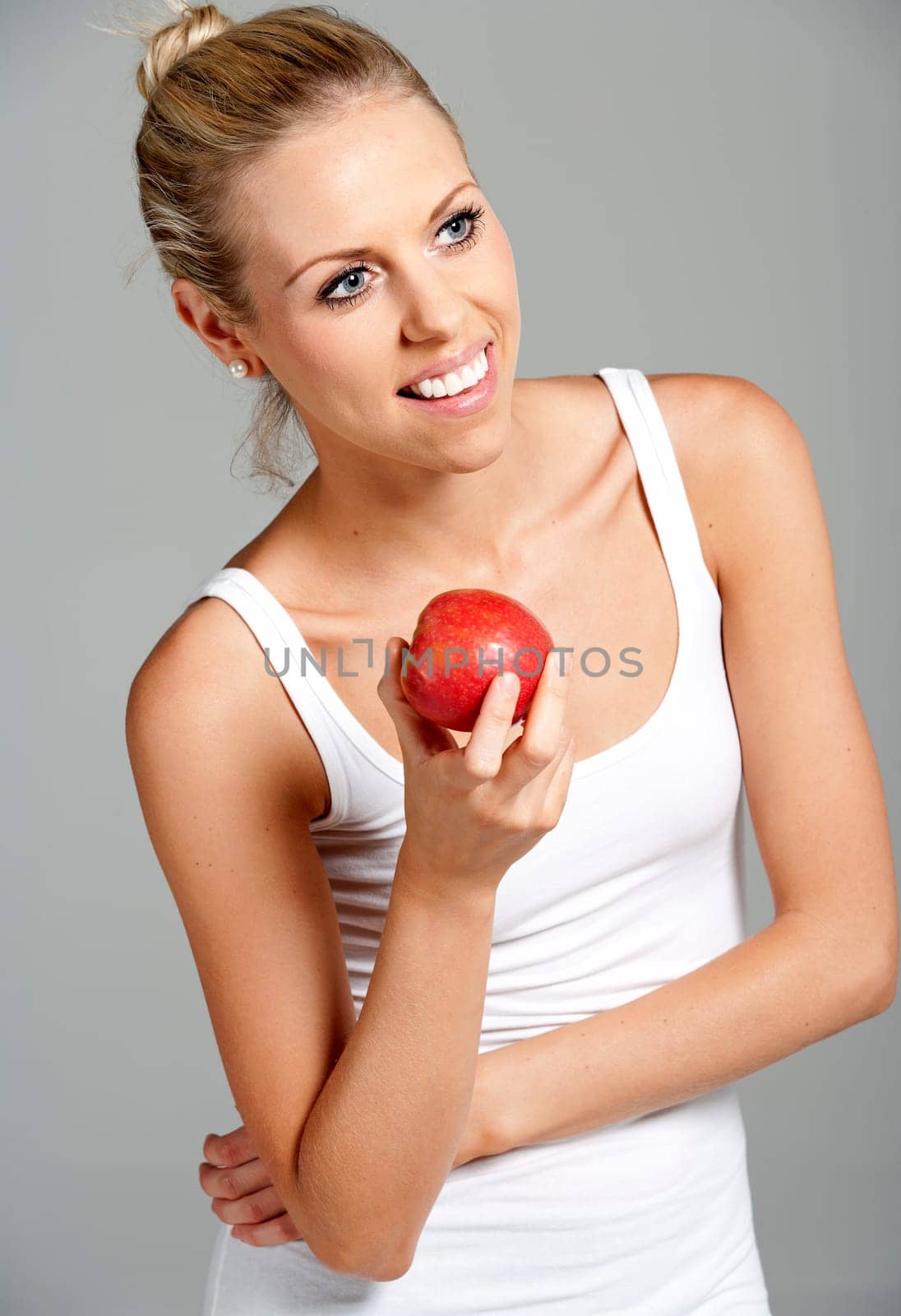 Beautiful young woman eating an apple wearing a white vest top