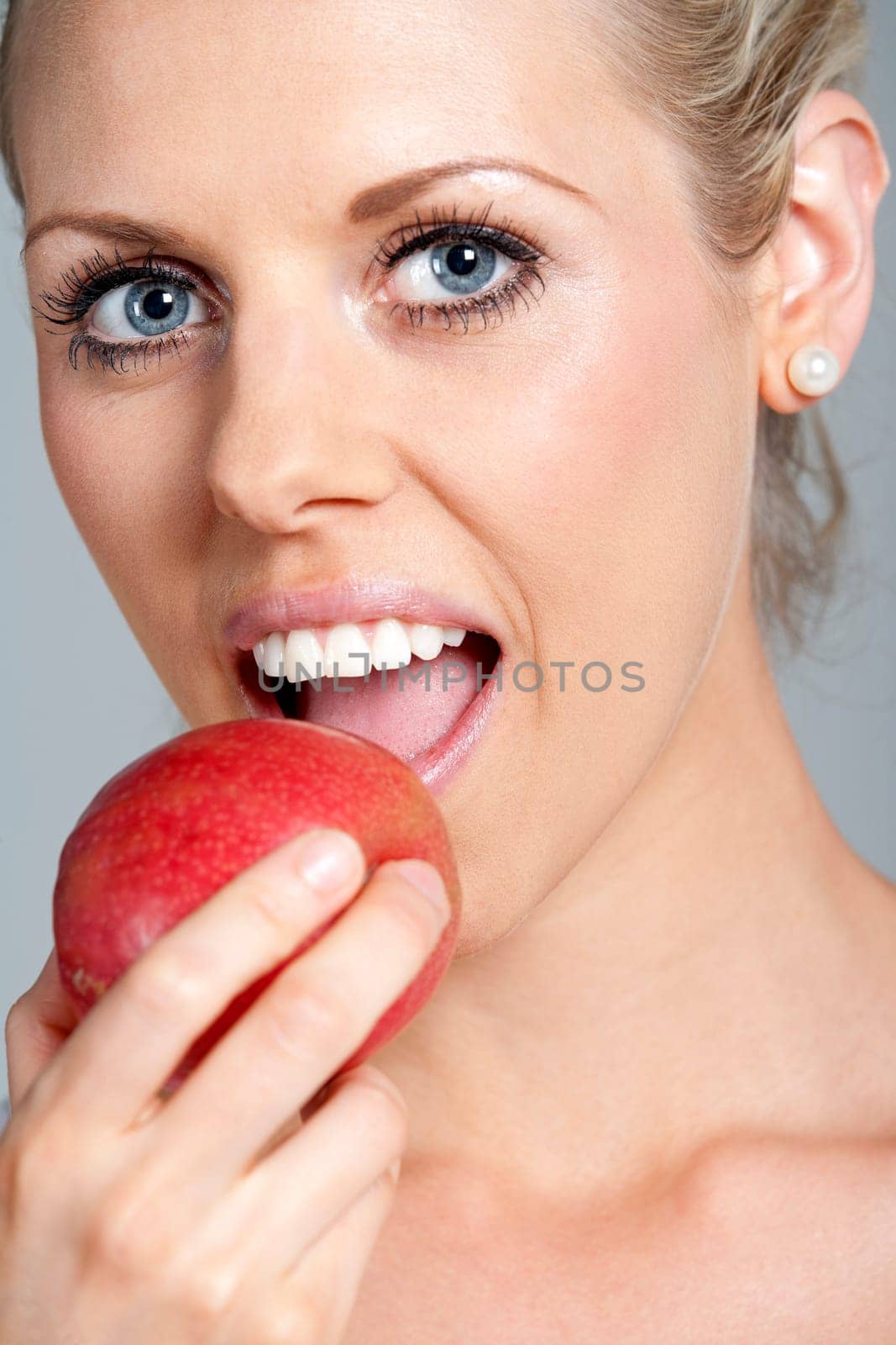 Beautiful young woman eating an apple wearing a white vest top