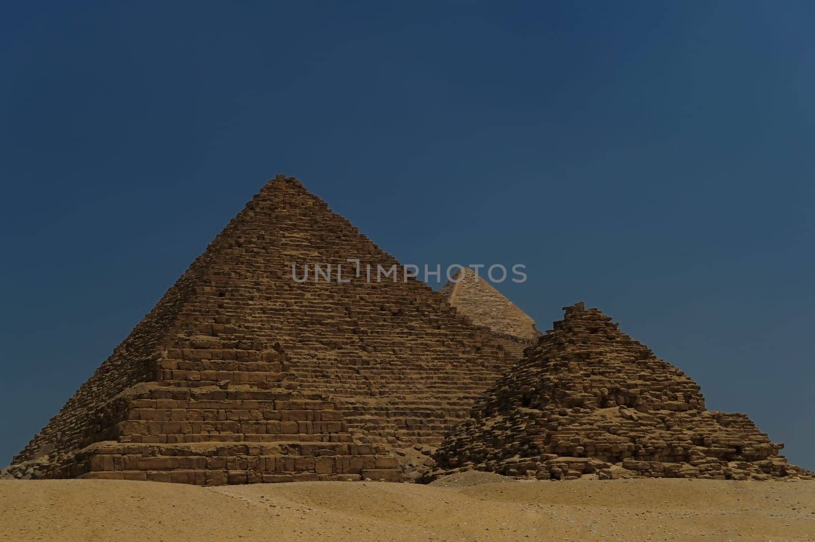 A row of camels transport tourists in front of all of the Giza Pyramids in Cairo, Egypt