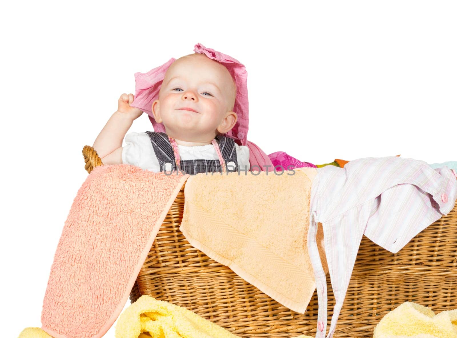 Impish little baby with a cute little self-satisfied expression sitting in amongst the washing in a wicker laundry basket