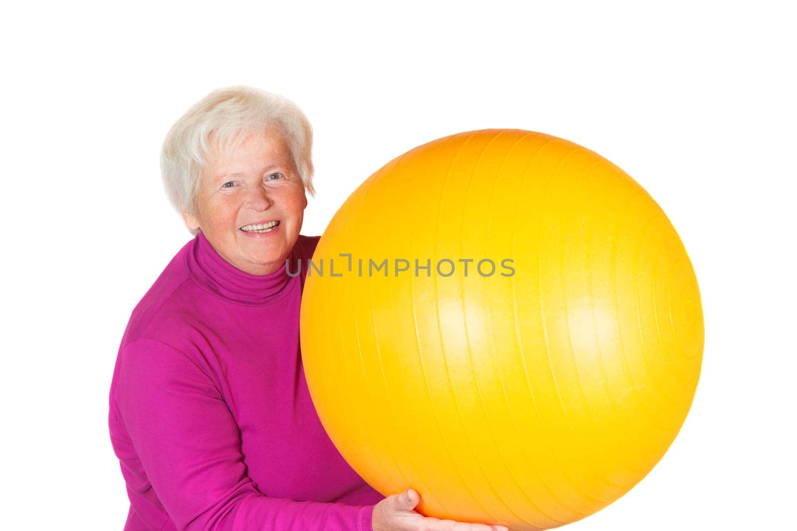Elderly senior woman holding a yellow pilates or gym ball in her hand with a lovely radiant smile on her face