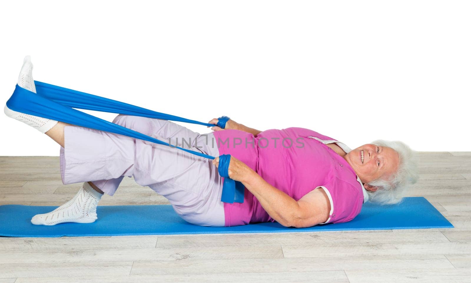 Overweight senior woman full of zest and vitality exercising on a gym mat with her leg raised in the air using a strap for leverage