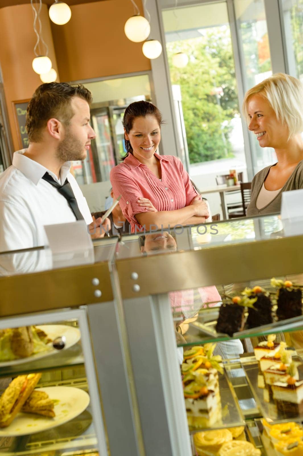 Waiter showing women cakes on window display cafe smiling friends
