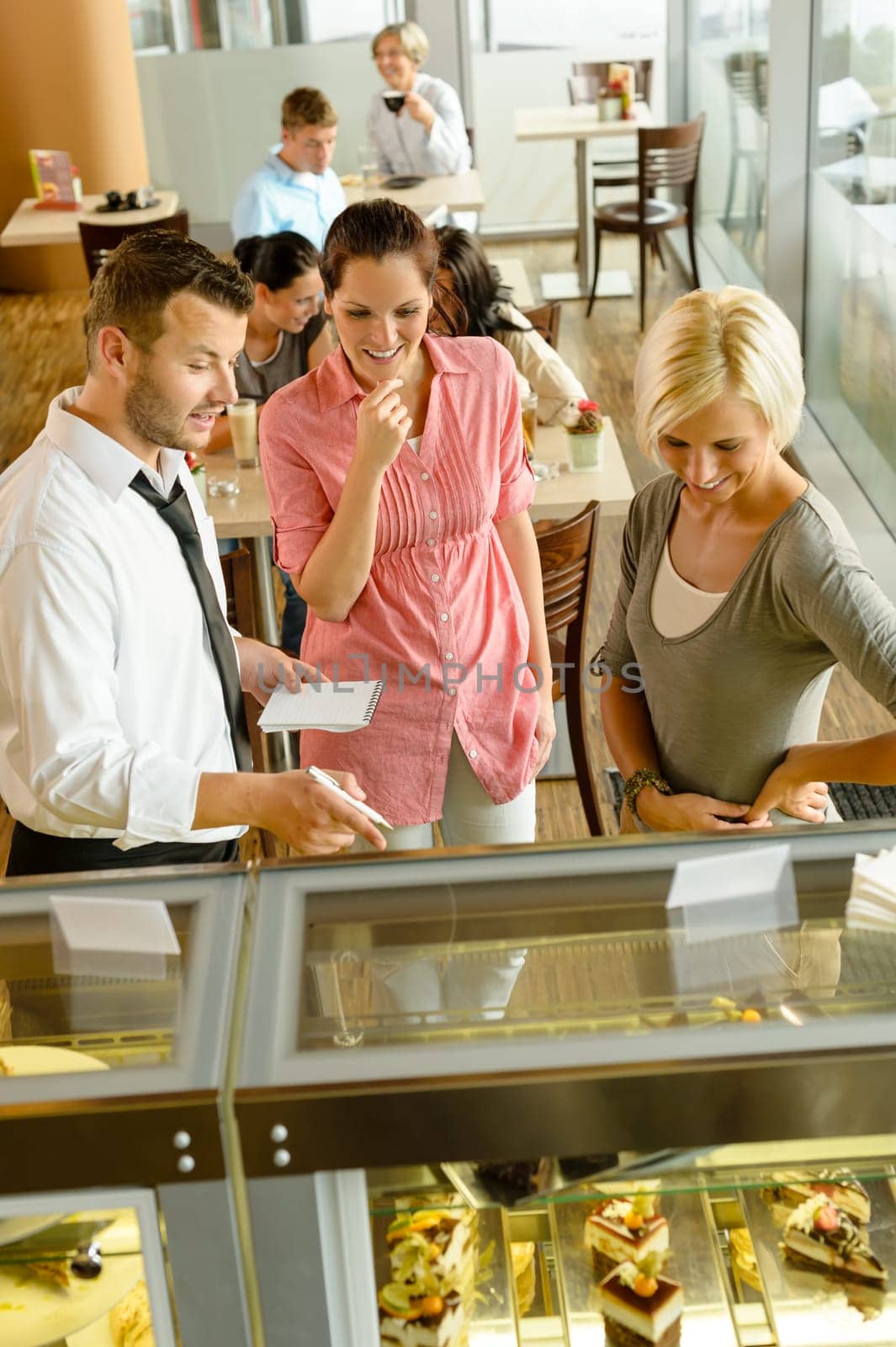 Waiter showing women cakes on window display cafe smiling friends
