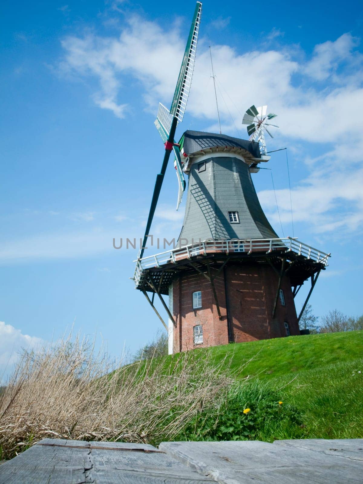 Windmill in East Frisia with wooden walkway in the foreground with blue sky with small white clouds