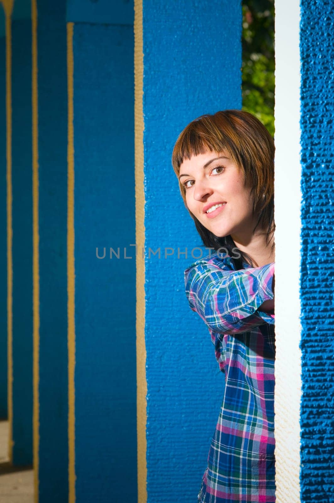 Upper body portrait of a young brunette woman posing between blue architectural pillars