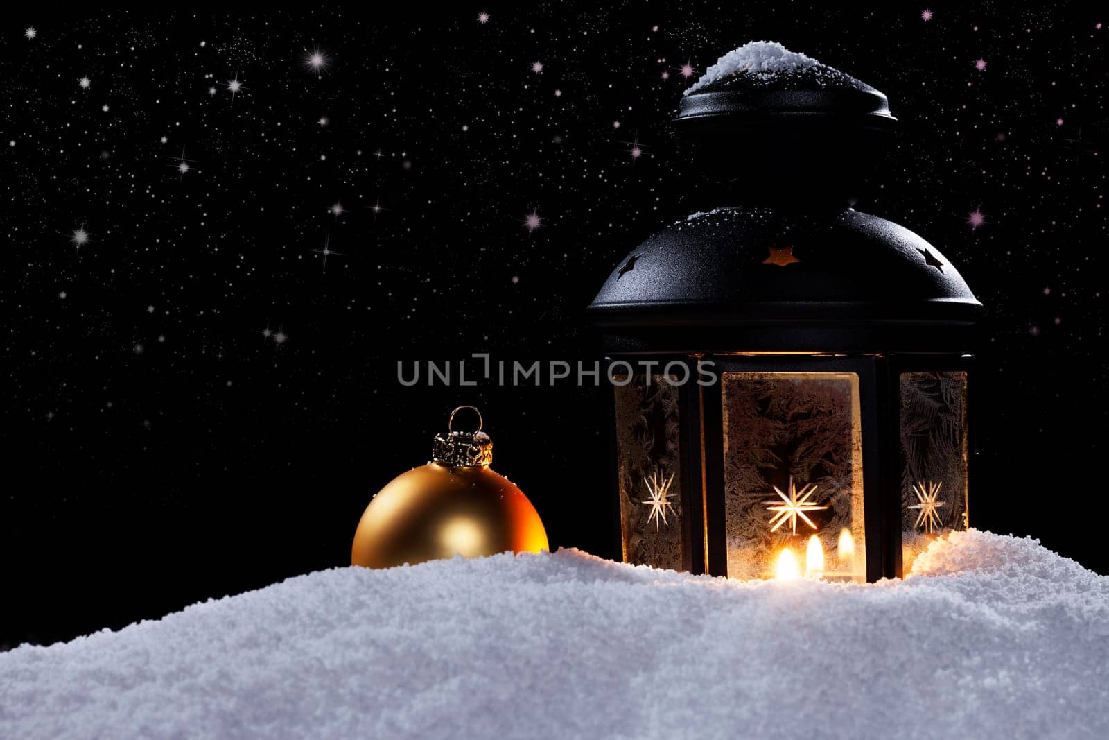 Lantern with Christmas bauble in the snow under starry sky