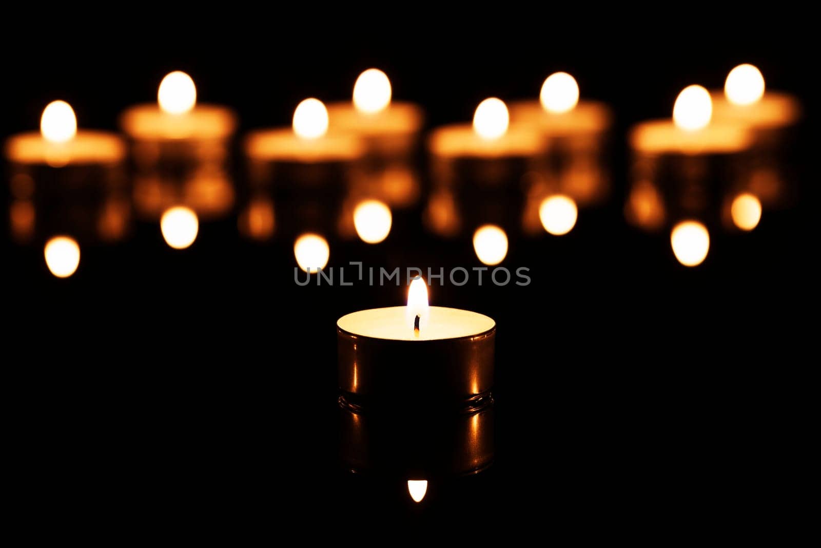 A tea light in front of many tea lights on black mirror