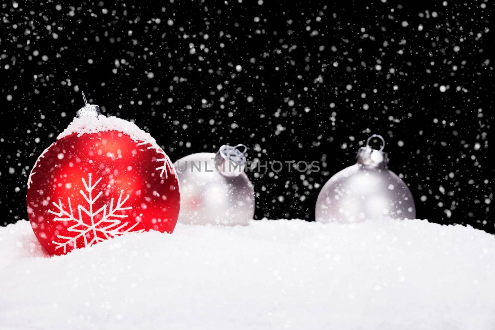 Christmas balls in the snow in snowfall against black background